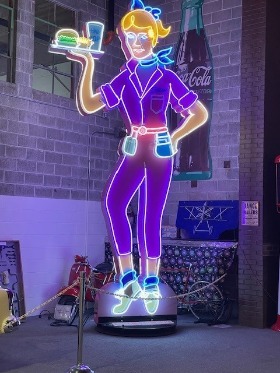 Neon light of a woman holding a platter of burgers and fries